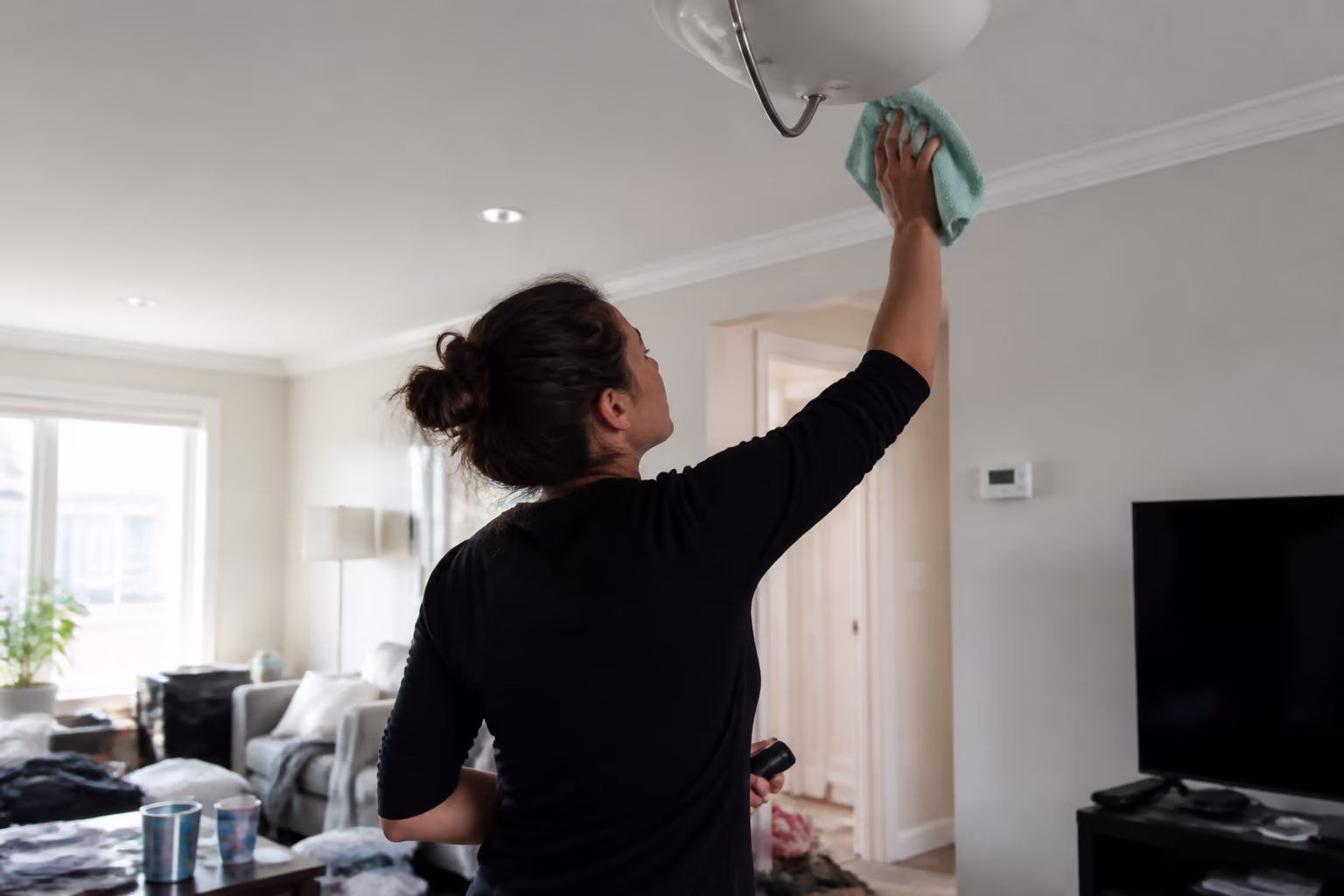 A cleaner working top-to-bottom in an Ottawa living room, dusting ceiling corners and light fixtures with a colour-coded microfibre cloth.