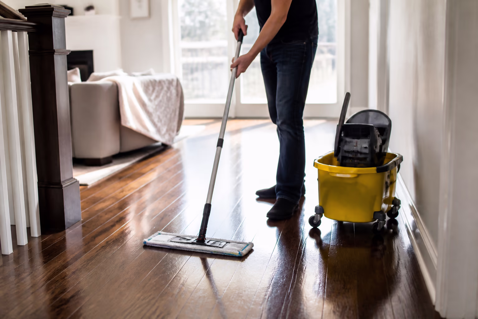 A mop and wheeled bucket standing on a freshly cleaned hardwood floor, soft afternoon light across the planks in an Ottawa home.