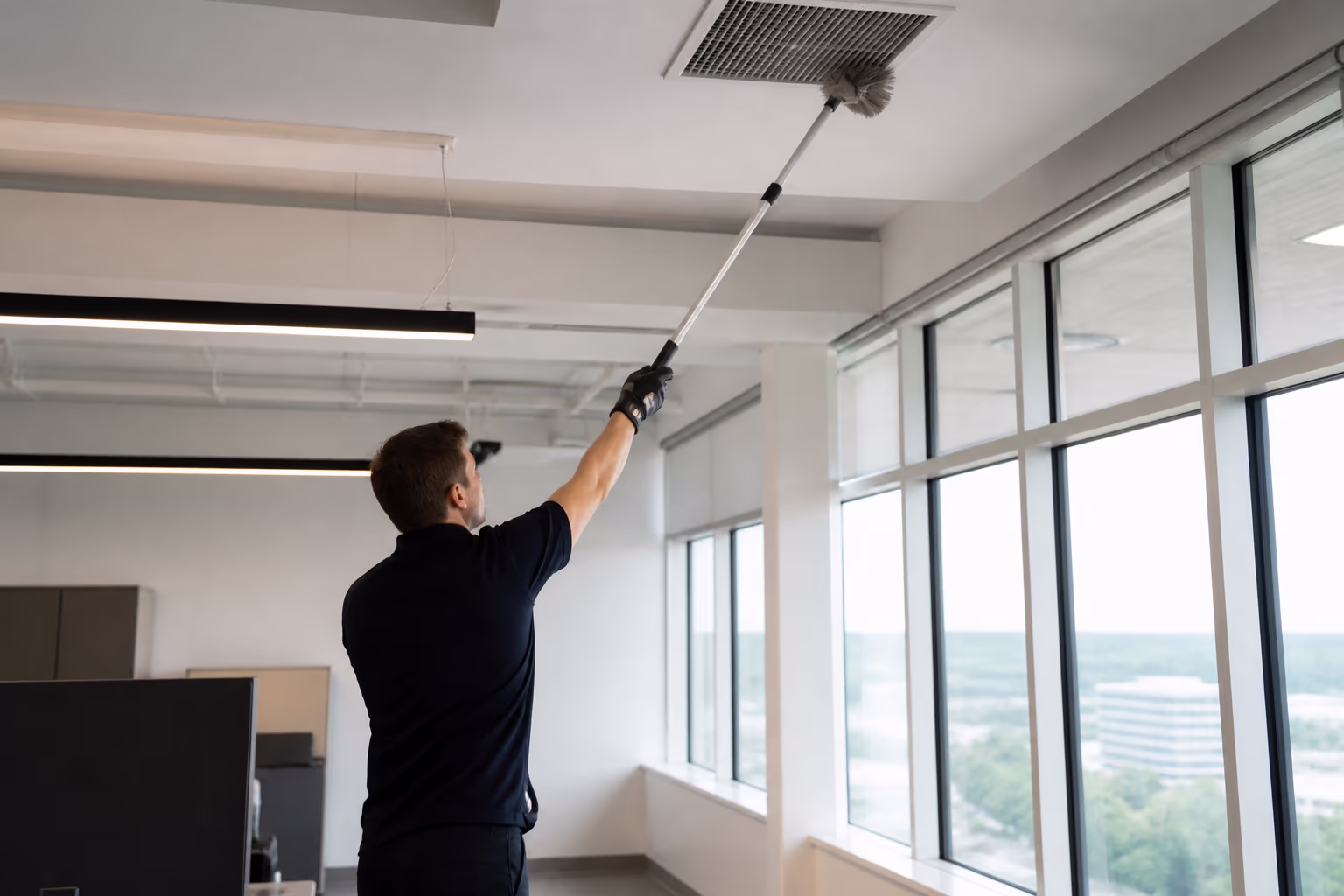 Commercial deep-cleaning technicians de-dusting high ceiling vents and window sills with extendable tools in a bright open-plan Ottawa office during an after-hours restoration.