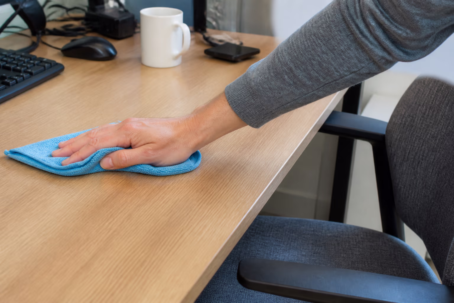 A close view of an open-plan Ottawa office desk beside a fabric chair and carpet edge, where dust and shed skin cells settle into fibres that a quick daily wipe never reaches.