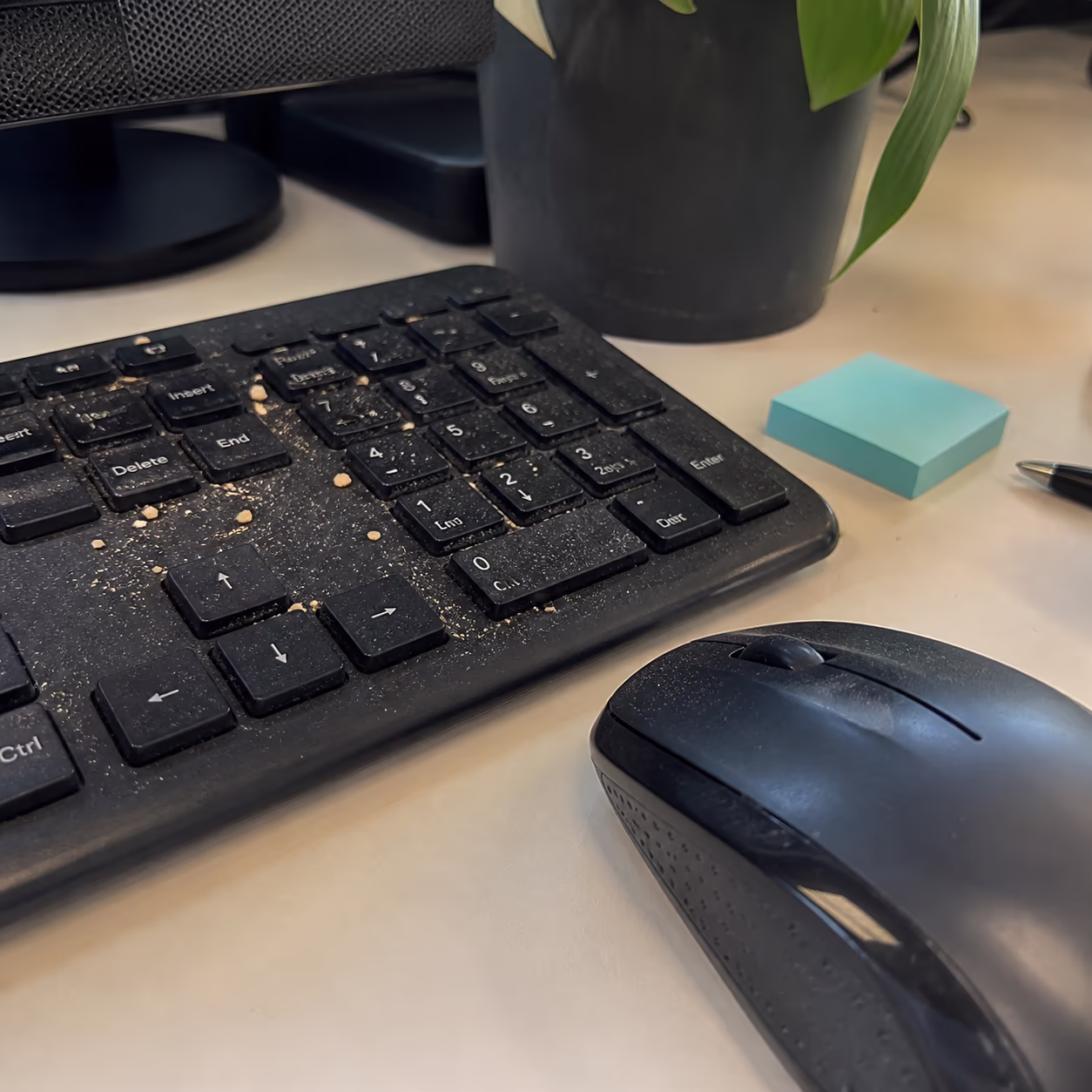 A close-up of a computer keyboard and mouse on a busy office desk, with crumbs and dust visible between the keys before a workstation clean in Ottawa.