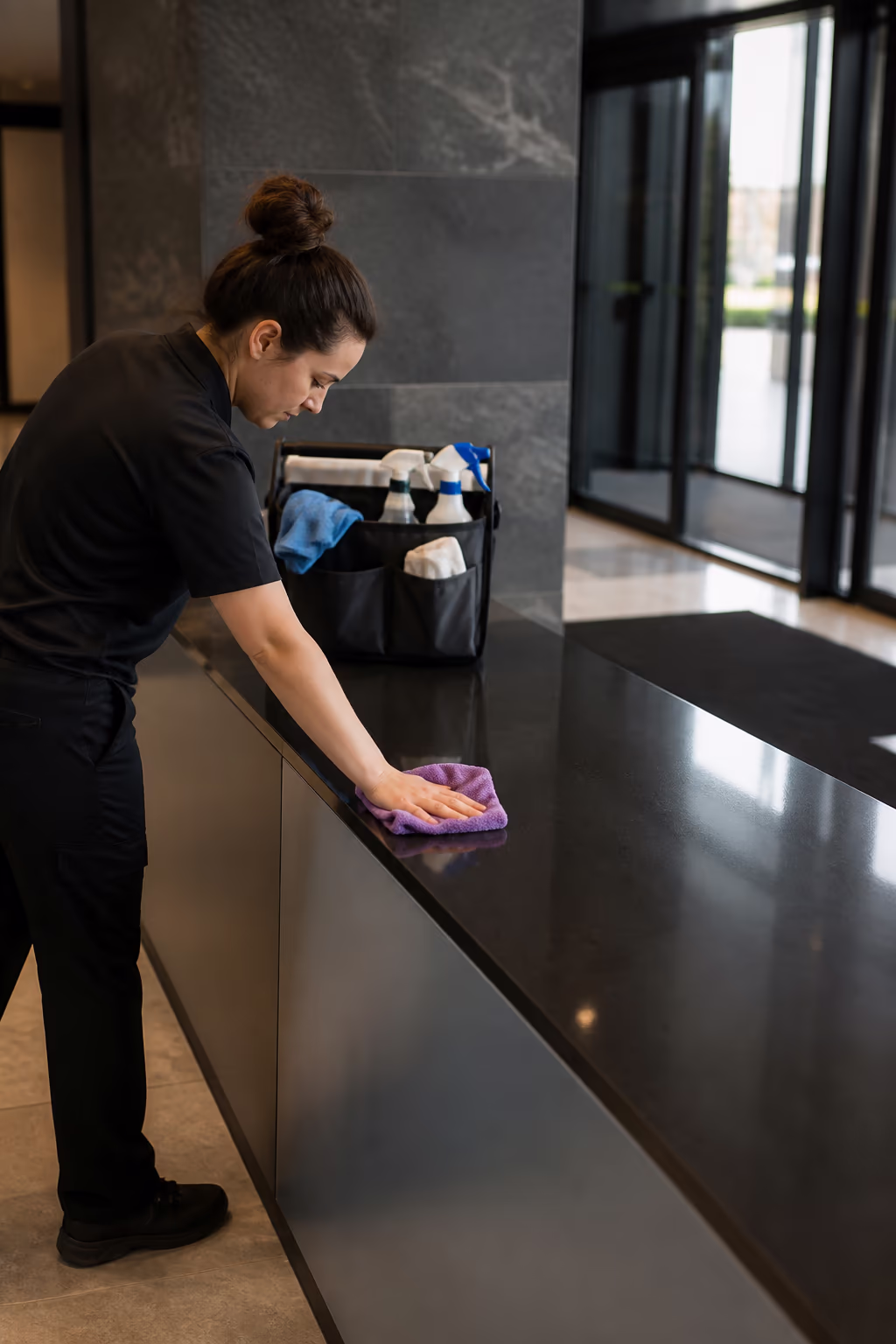 A neat row of restocked commercial washroom supplies, microfibre cloths and a cleaning caddy standing ready beside a polished lobby entrance in an Ottawa office tower, showing the continuous daytime readiness a day porter provides.