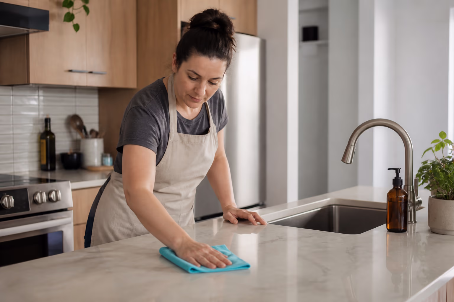A cleaner in an apron and yellow gloves holding a caddy of cloths and food-safe cleaning bottles in a bright Ottawa kitchen.