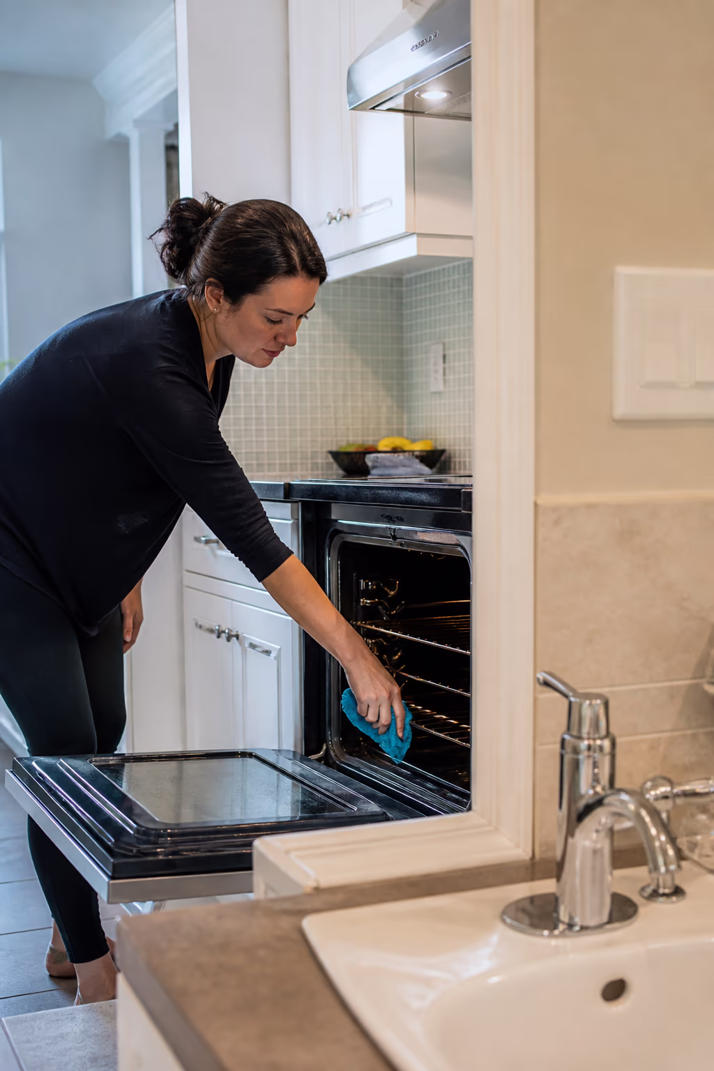 A deep-cleaned Ottawa kitchen with a freshly scrubbed oven interior and degreased range hood, beside a bathroom sink with a descaled faucet and restored grout, ready for the next regular maintenance cycle.