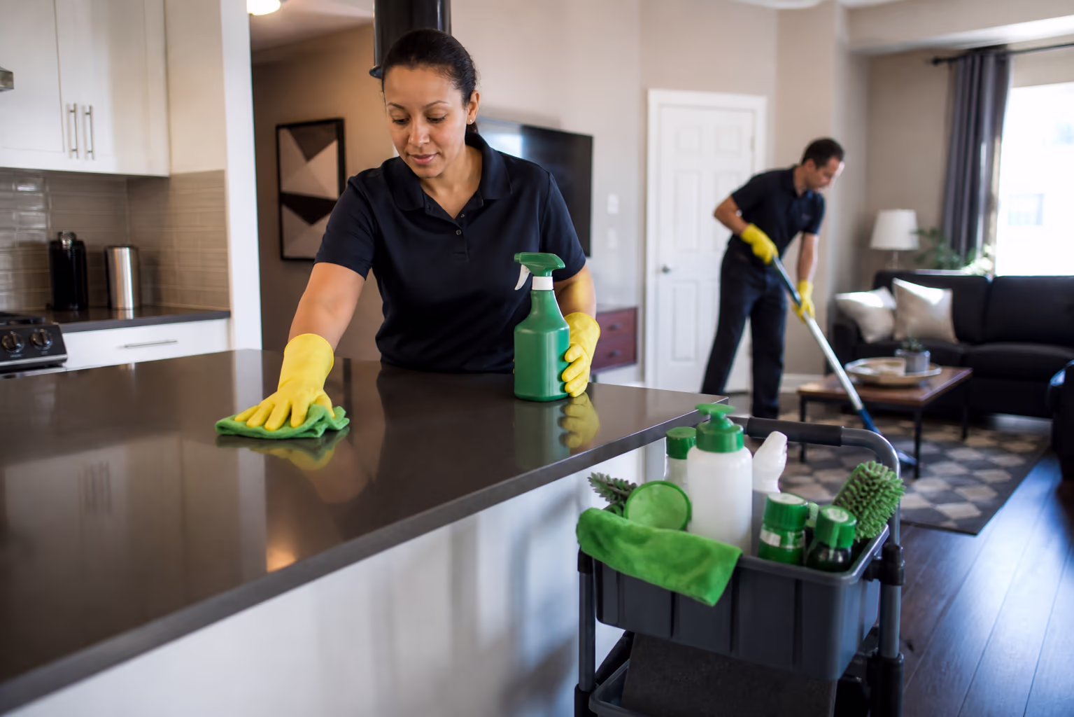 Cleaning technicians in uniform and yellow gloves cleaning a kitchen island and living room with green supplies during a residential visit in Ottawa.