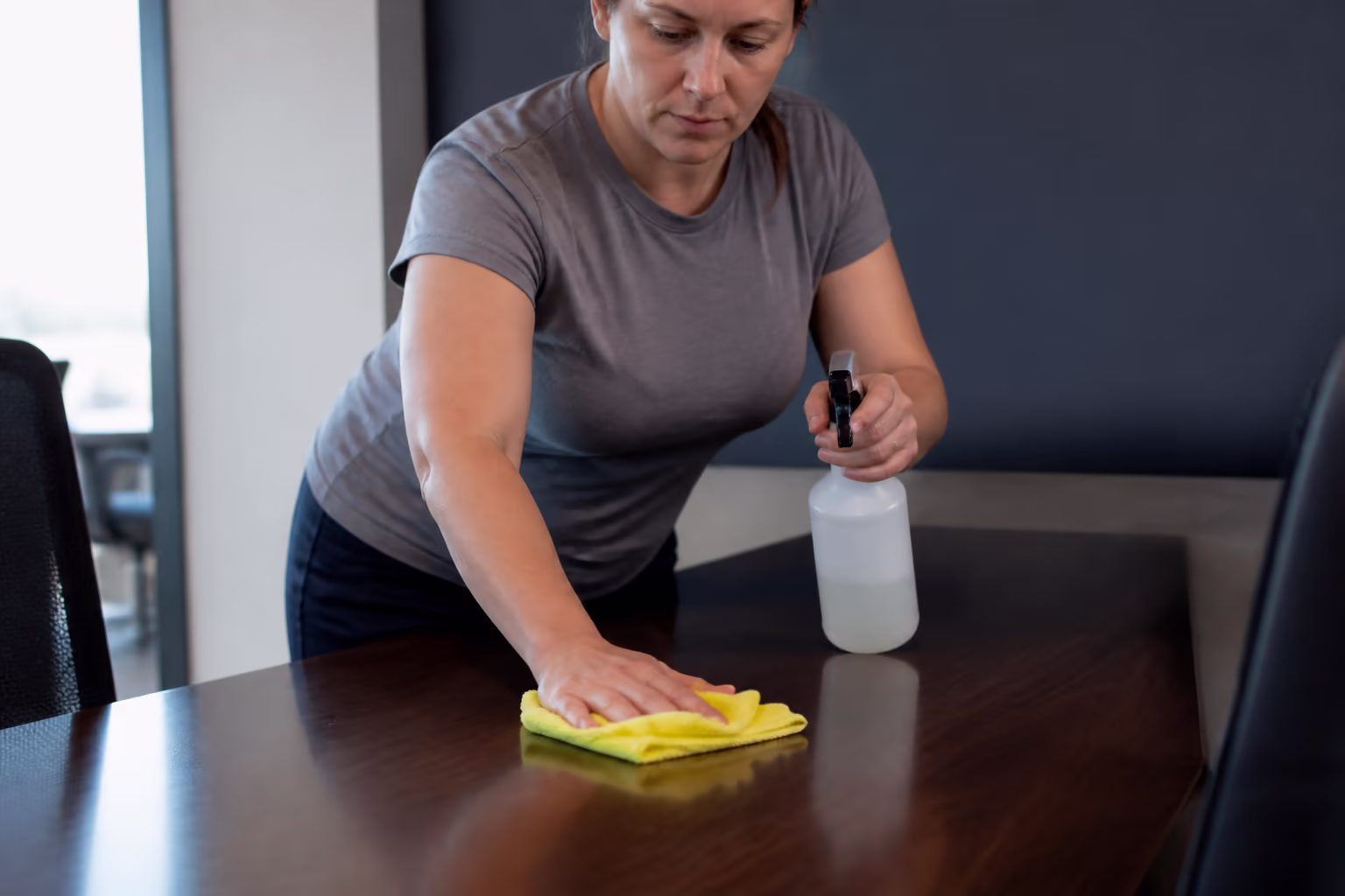 A professional cleaner holding a spray bottle and a microfibre cloth, preparing to clean surfaces in a bright Ottawa commercial workspace.