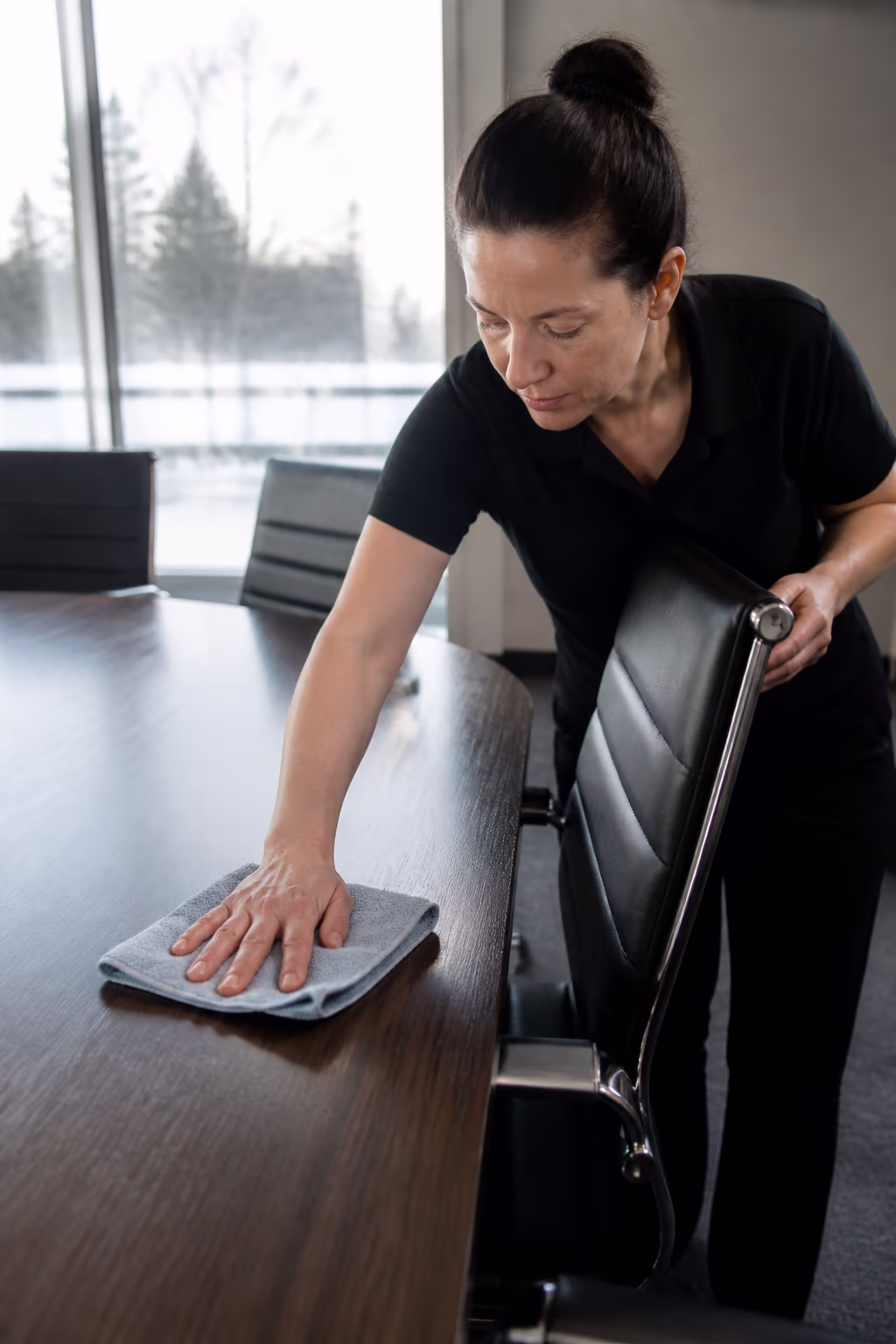 A cleaning technician conditioning a leather executive chair and dusting a fine hardwood boardroom table with soft microfibre cloths in a bright Ottawa boardroom.