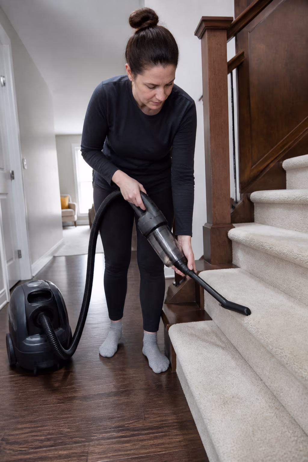 A portrait of a cleaner running a handheld vacuum attachment along the edge of a stair and carpet in an Ottawa home, then emptying the bin as part of a scheduled vacuum maintenance routine.