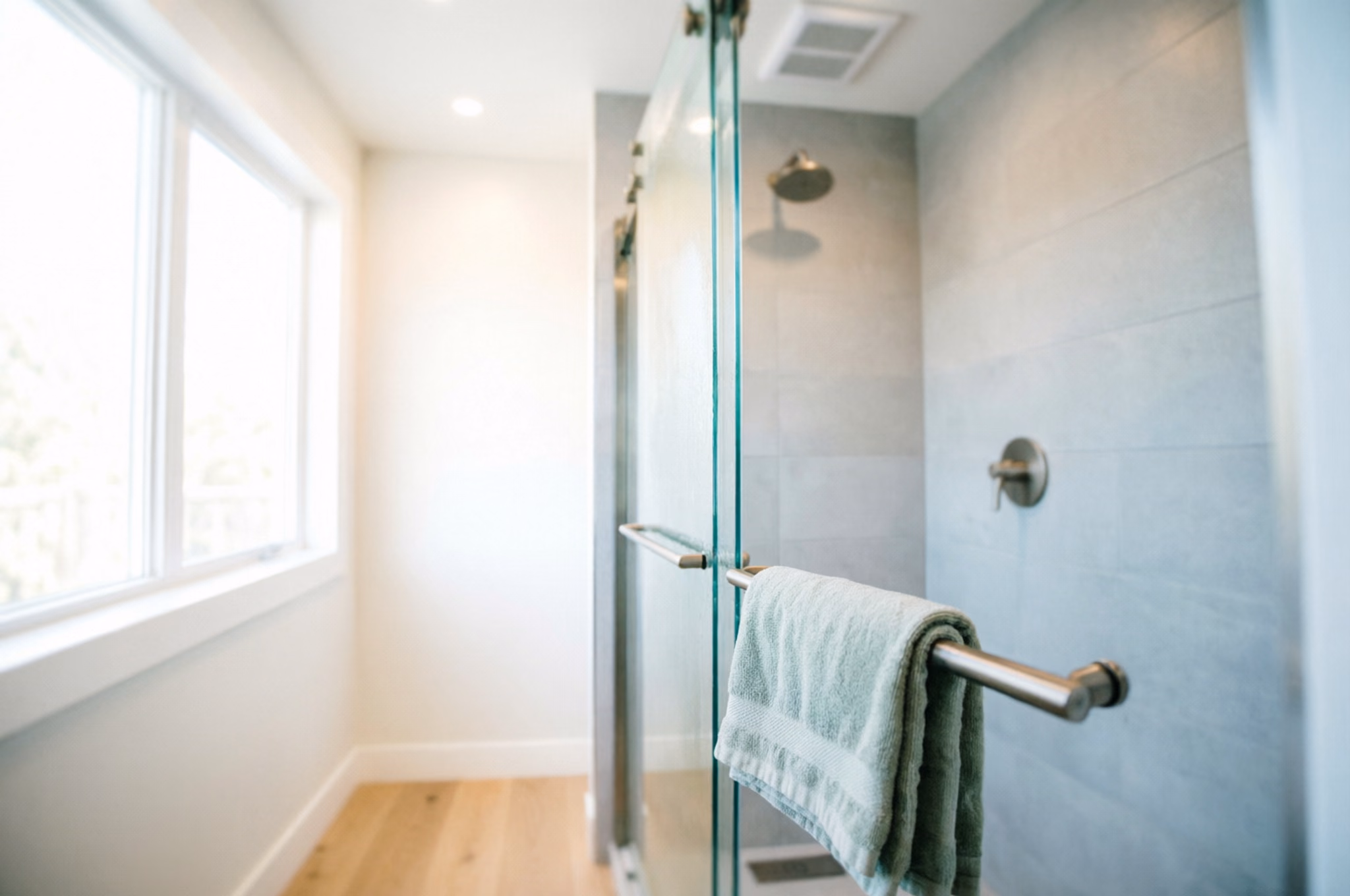 A portrait of a bright Ottawa shower with a clear, freshly cleaned glass door, a squeegee left on the rail and a clean towel folded on the edge.