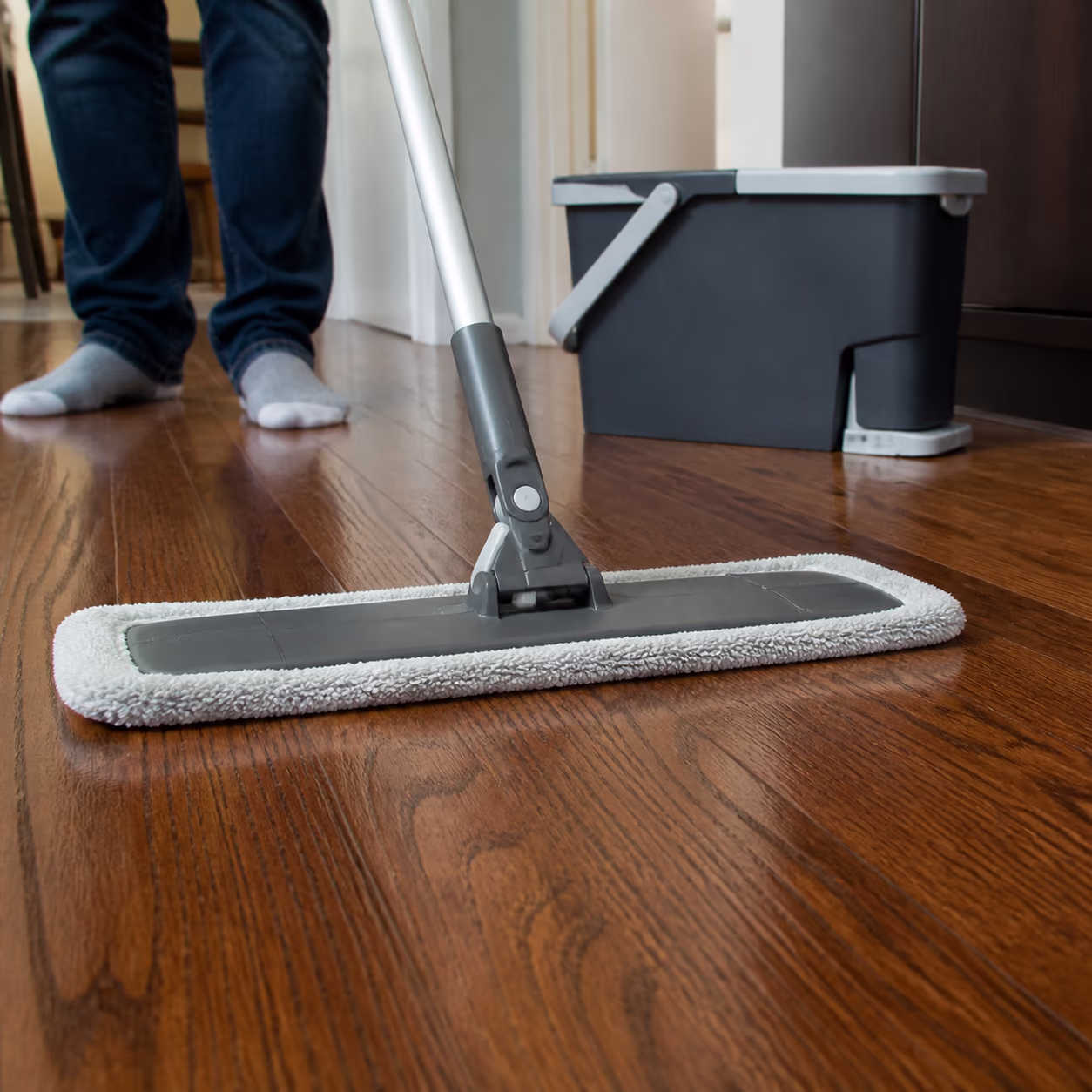 A close-up of a barely damp microfiber mop head resting on a warm hardwood floor in an Ottawa home, showing the damp-pass technique in the direction of the grain.