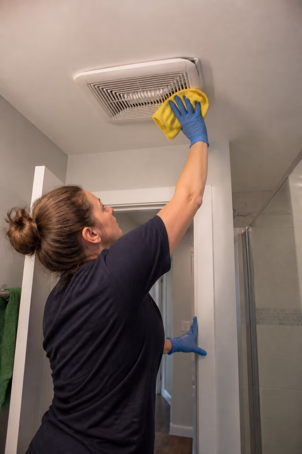 A cleaner wiping down a bathroom exhaust fan vent in an Ottawa home, controlling the moisture that makes rooms smell musty.