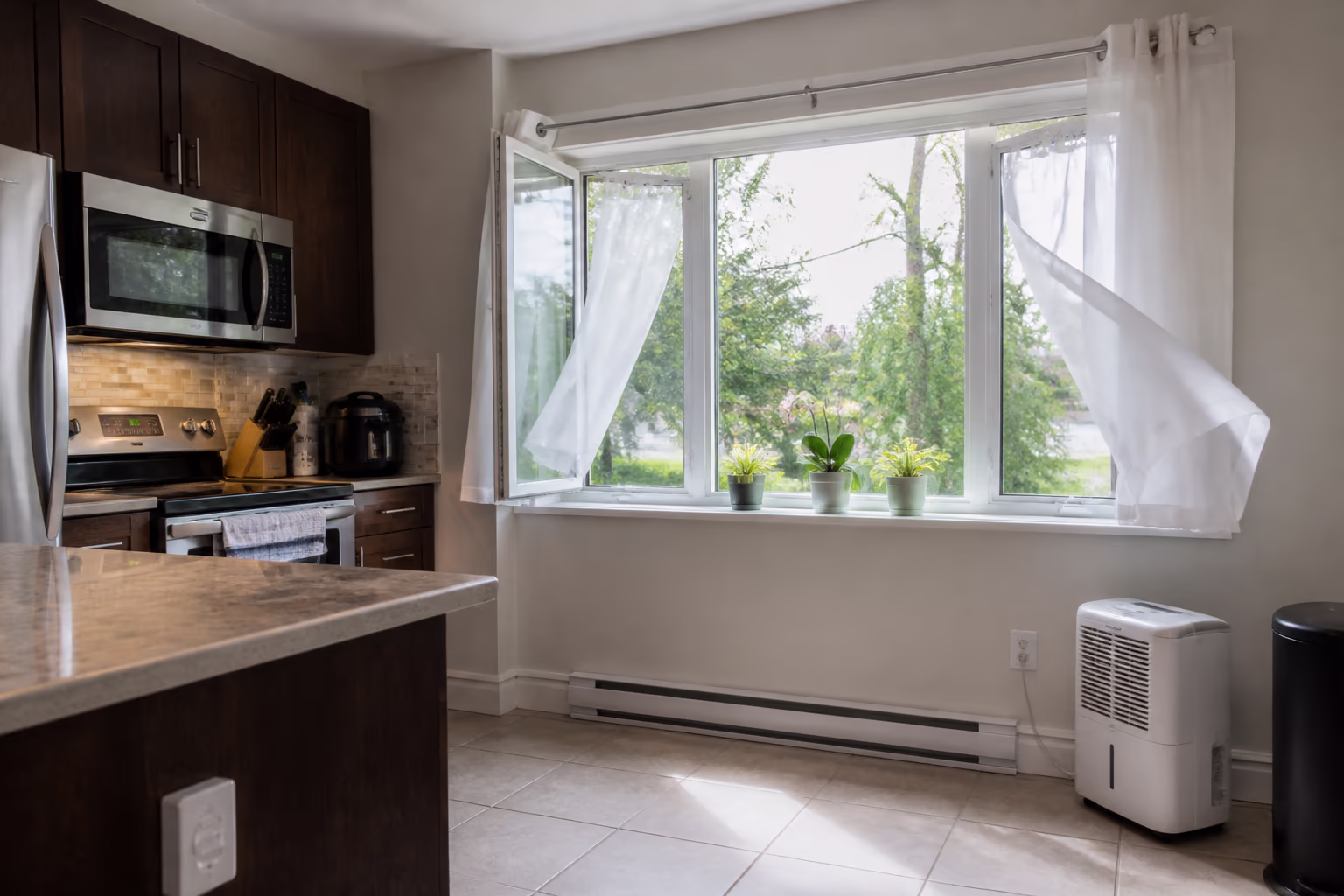 A wide view of an open kitchen window in an Ottawa home with a cross breeze moving fresh air through the room and a small dehumidifier beside the baseboard.