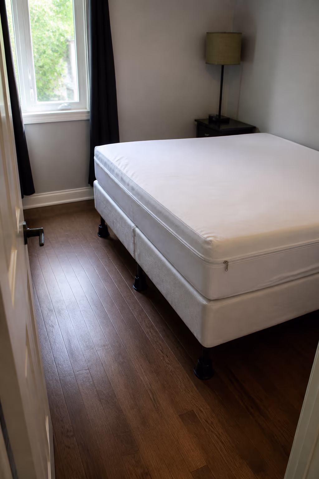 A portrait of a freshly prepared Ottawa bedroom after bed bug prep, the mattress and box spring sealed in zippered encasements, the bed pulled clear of the wall and the floor decluttered and ready for the licensed professional treatment.