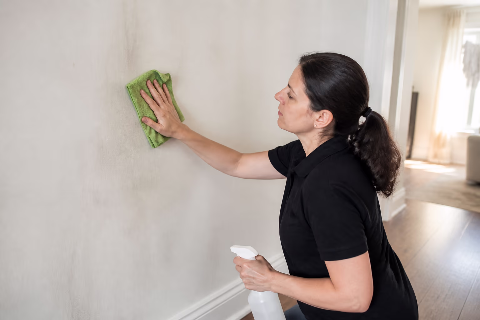 A cleaning technician in an Ottawa home wiping a smoke-residue-stained wall with a microfibre cloth and spray cleaner during a smoke odour deep clean.