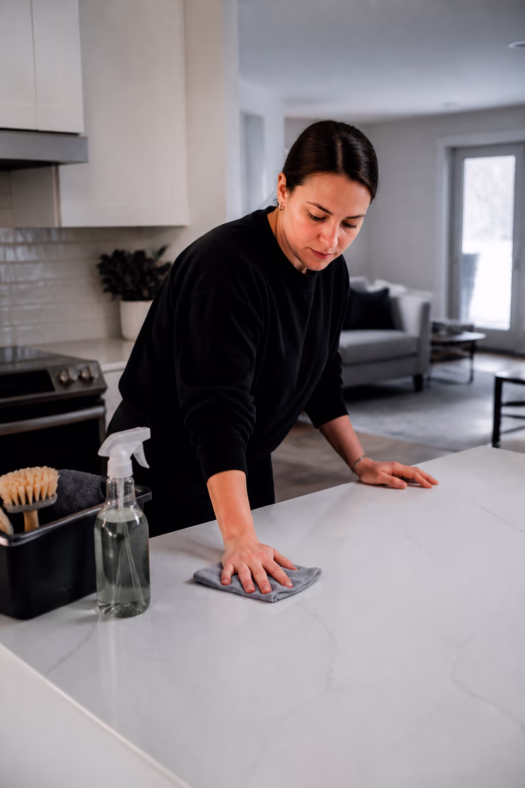A portrait of a cleaner finishing a thorough kitchen clean in an Ottawa home, wiping a counter with a cloth as a spray bottle of natural cleaner and a caddy sit nearby.