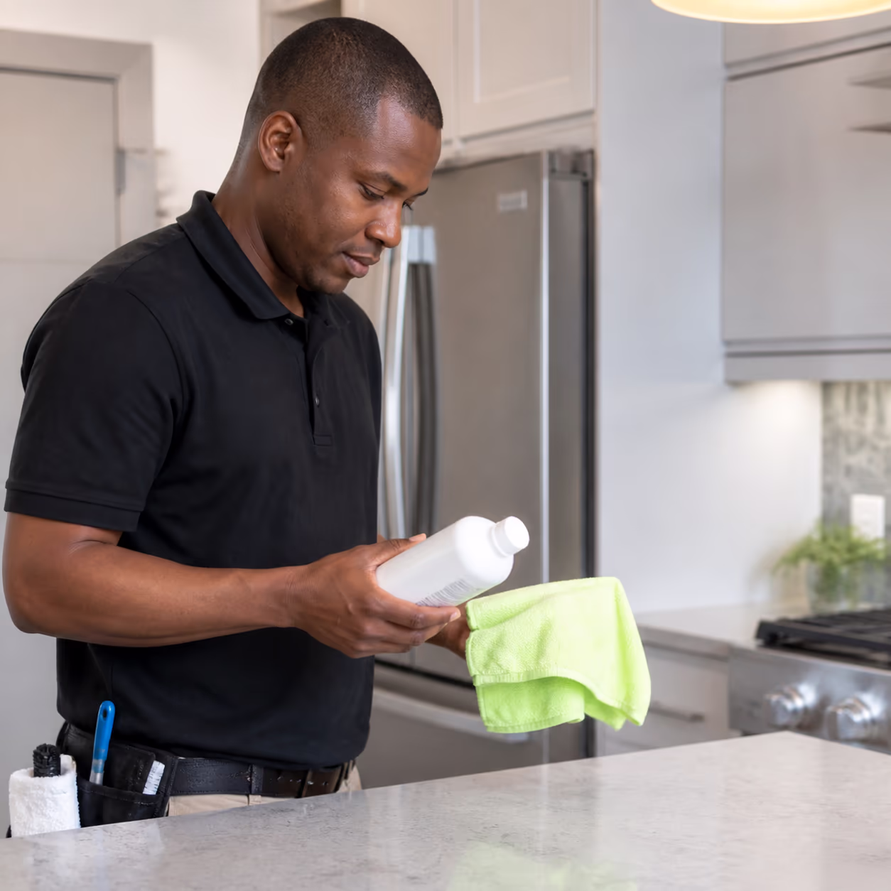 A close view of a professional cleaner choosing a product and microfibre cloth for a delicate kitchen countertop during a residential clean in a bright Ottawa home.