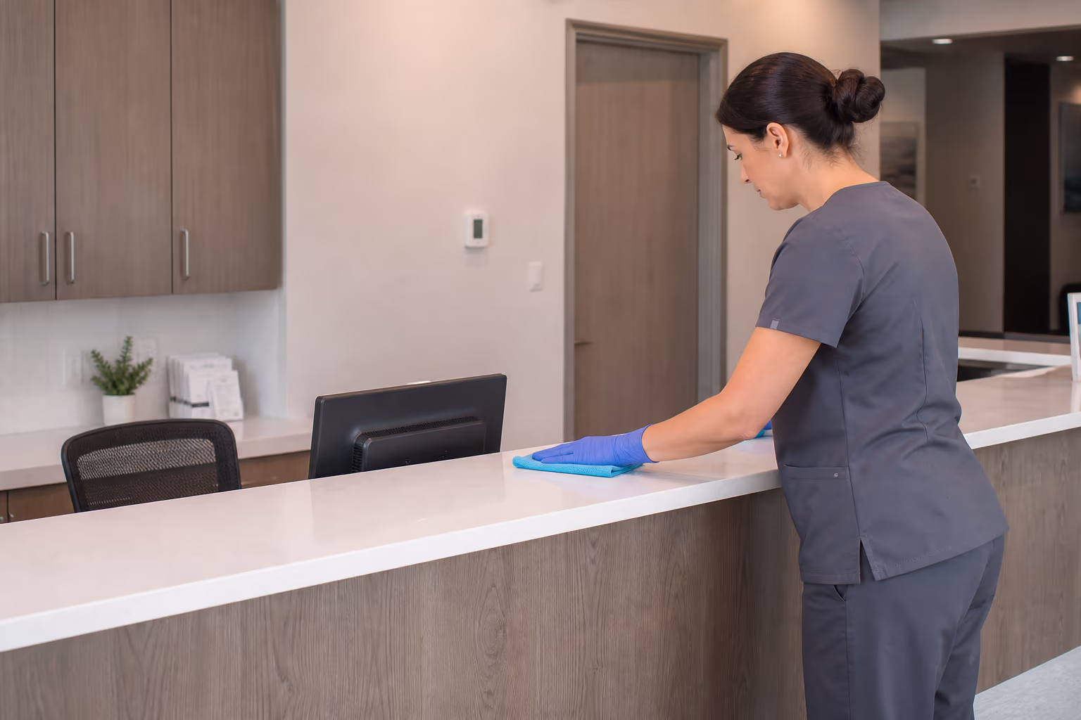 A professional cleaning team member in uniform disinfecting the high-touch surfaces of a bright Ottawa medical office, wiping a reception counter with a microfibre cloth.