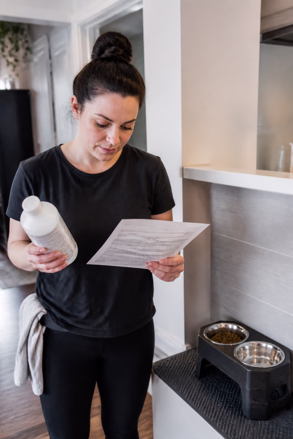 A portrait of a cleaning technician reading a cleaning product label and safety data sheet before wiping a pet food station in an Ottawa home.
