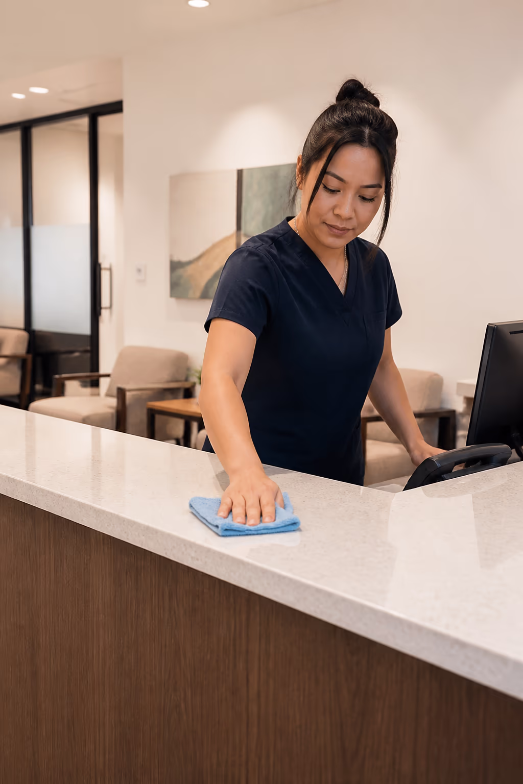 A professional cleaner wiping a reception front desk and shared touchpoints in a bright Ottawa office, with clean fabric seating and a tidy wayfinding sign behind.