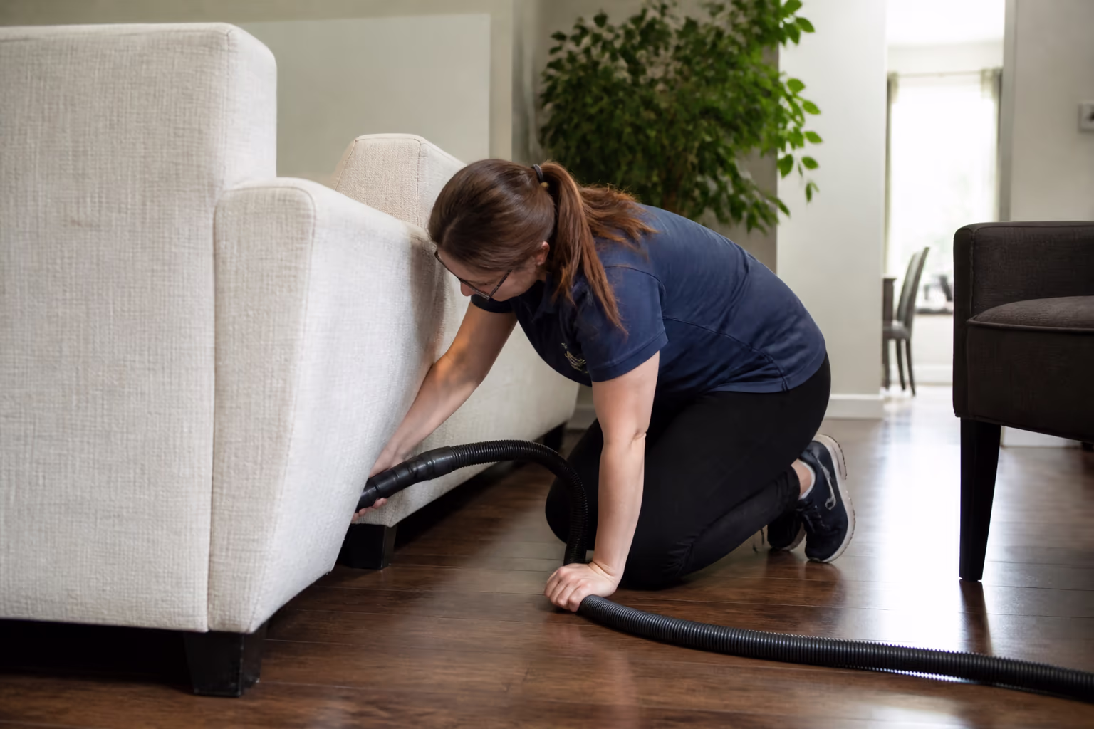 A landscape view of a professional cleaner reaching behind and under furniture during a planned deep clean in an Ottawa home, showing the deeper work that earns its own visit.