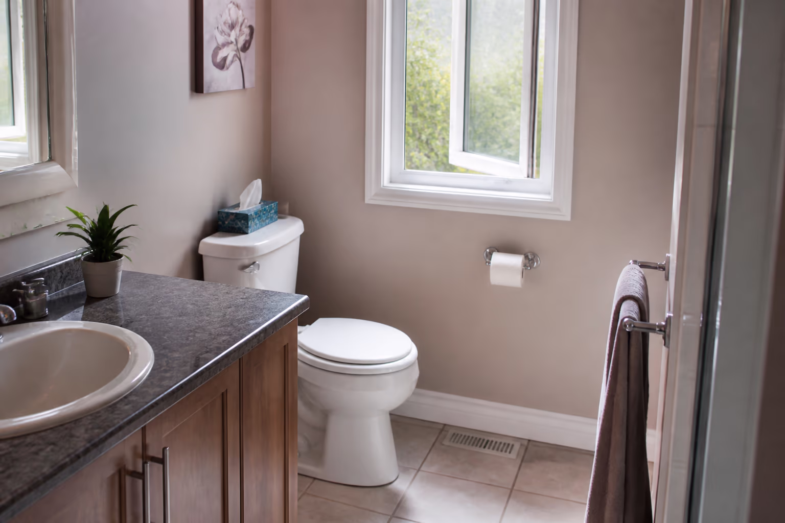 A landscape view of a fresh, tidy Ottawa bathroom after a clean, the toilet, mirror and floor spotless and a window cracked to vent the room, showing how airflow keeps a bathroom fresh between cleanings.