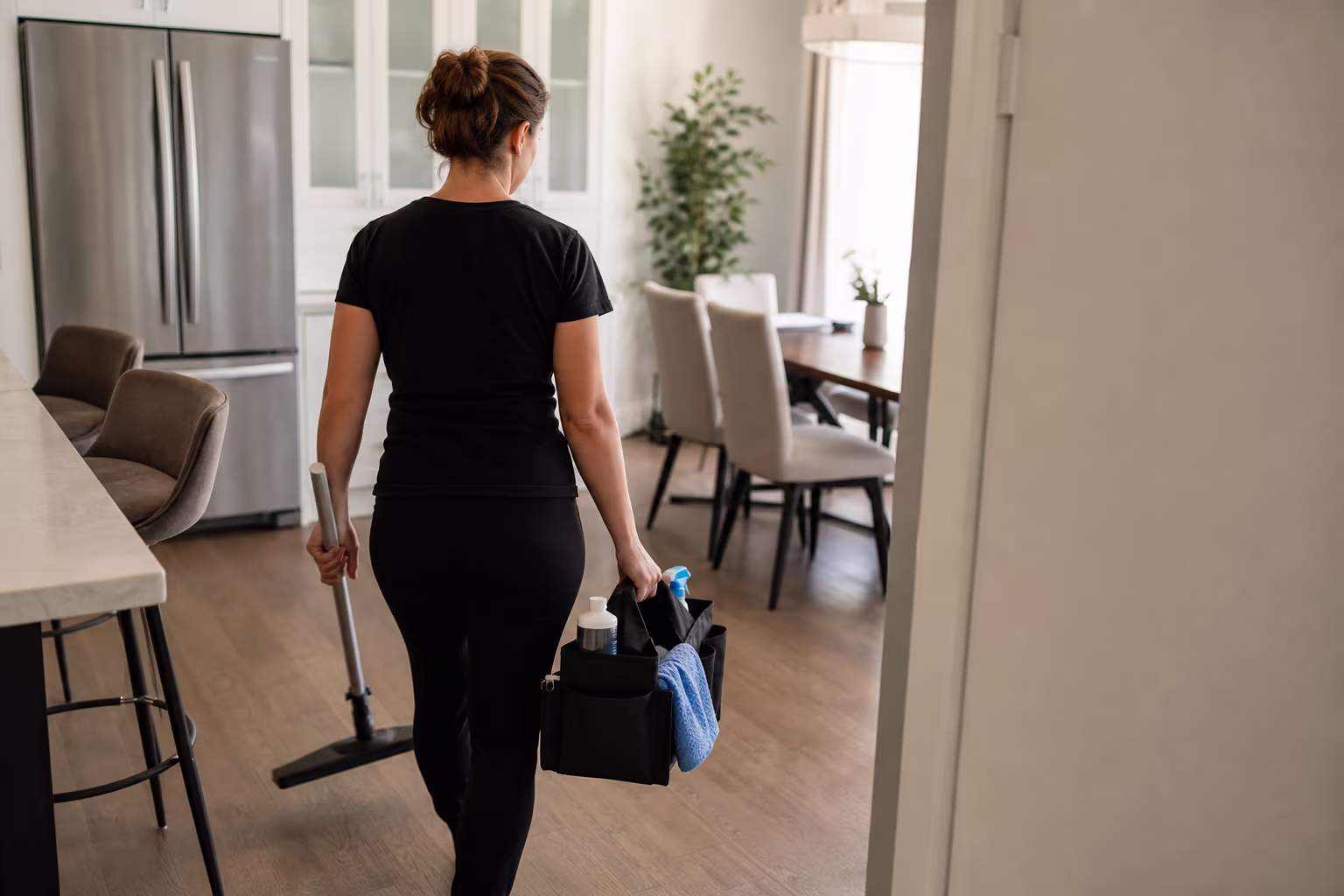 Cleaner carrying a supply caddy through a bright condo suite