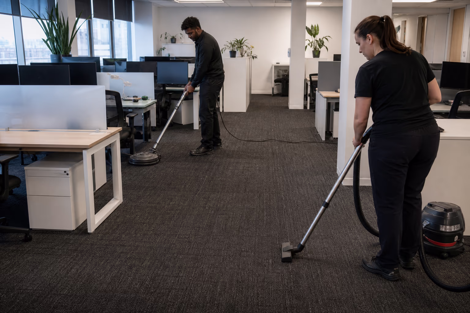 Two cleaners servicing an open-plan office