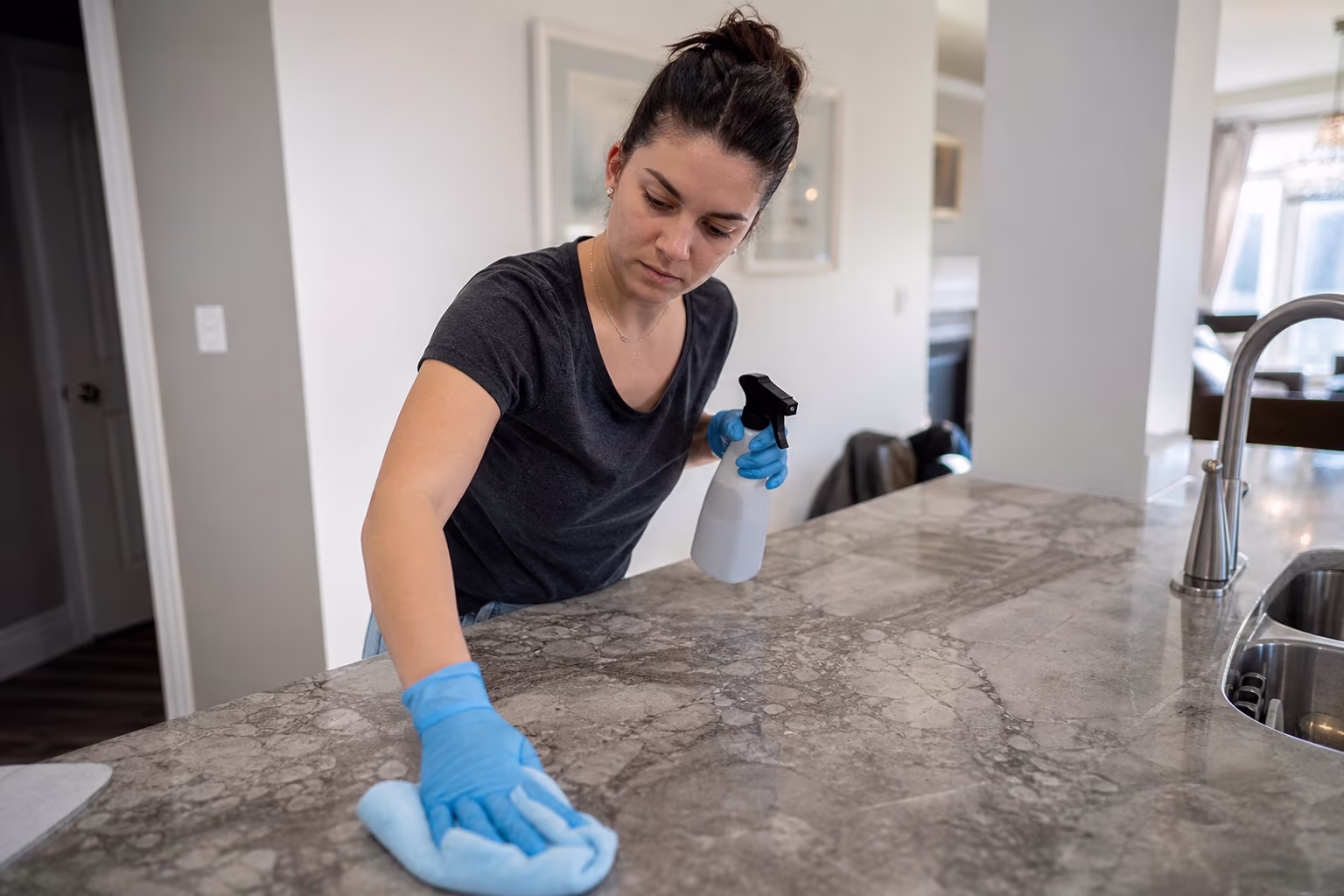 Cleaner wearing gloves and holding a spray bottle and cloth in a home