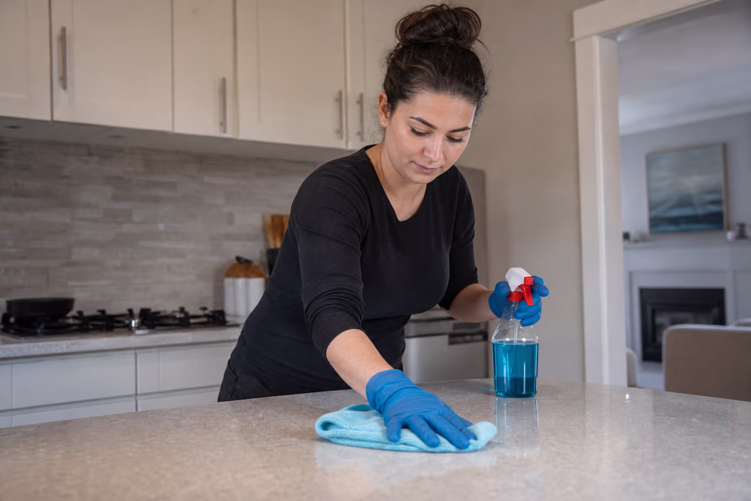 Cleaner wearing gloves and holding a spray bottle and cloth in a home