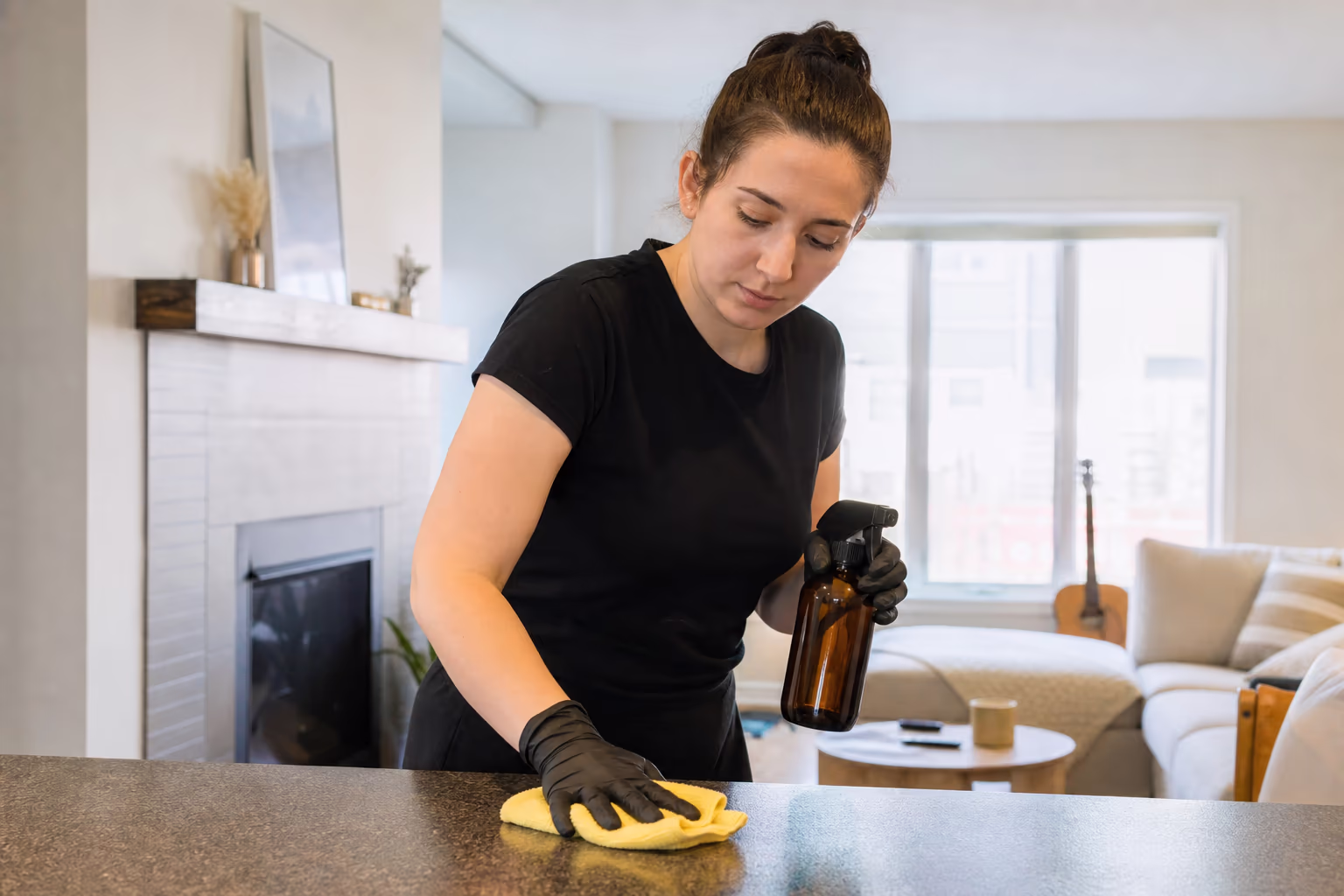 Cleaner wearing gloves and holding a spray bottle and cloth in a home