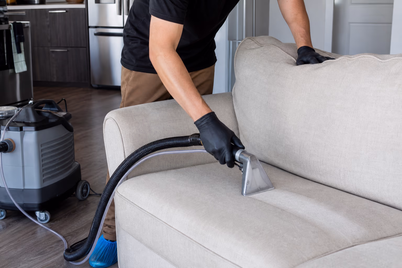 Gloved hands using an upholstery extractor on a light-coloured sofa