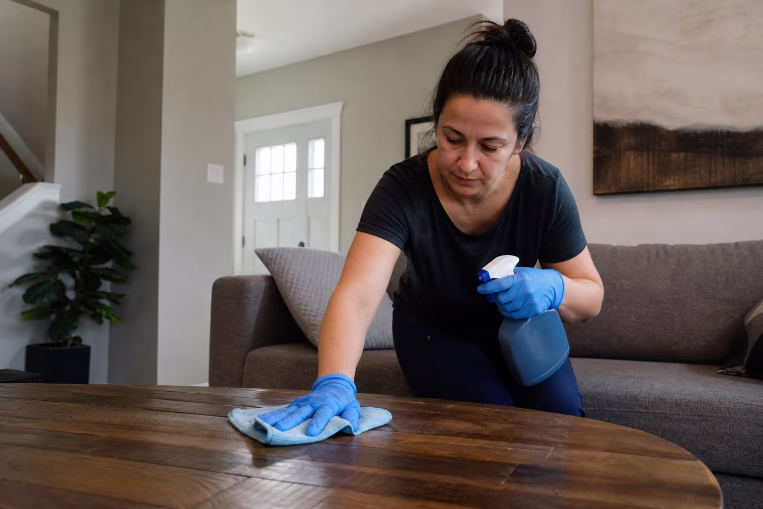 Cleaner wearing gloves and holding a spray bottle and cloth